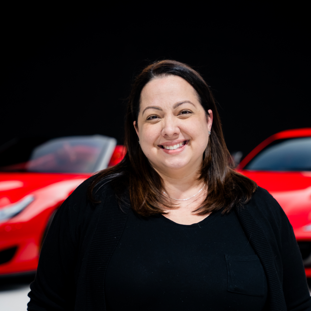 17png | Txtcharlie Smiling woman with dark hair in black top, background shows a red car and dark sky.