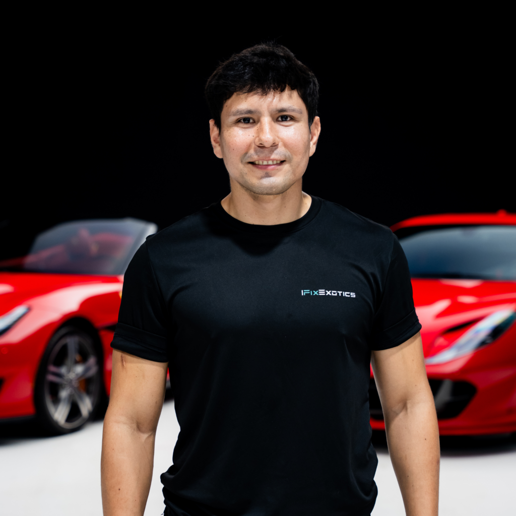 24png | Txtcharlie Man in a black t-shirt standing in front of red cars, posing for a photo in a showroom.