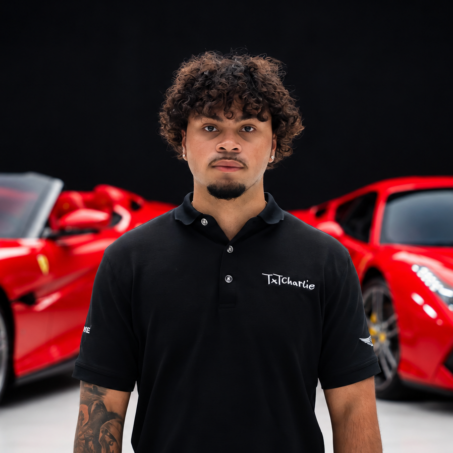 Christiandortapng | Txtcharlie Portrait of a young man with curly hair and a goatee, wearing a black polo with a 'TxCharlie' logo, standing in front of red sports cars.