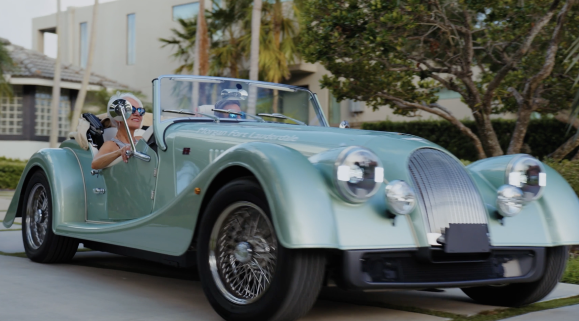 Screenshot 20260908 at 52245 Pm | Txtcharlie Two people ride in a vintage teal convertible driving down a suburban street; driver wears sunglasses and smiles, passenger in the passenger seat also visible.
