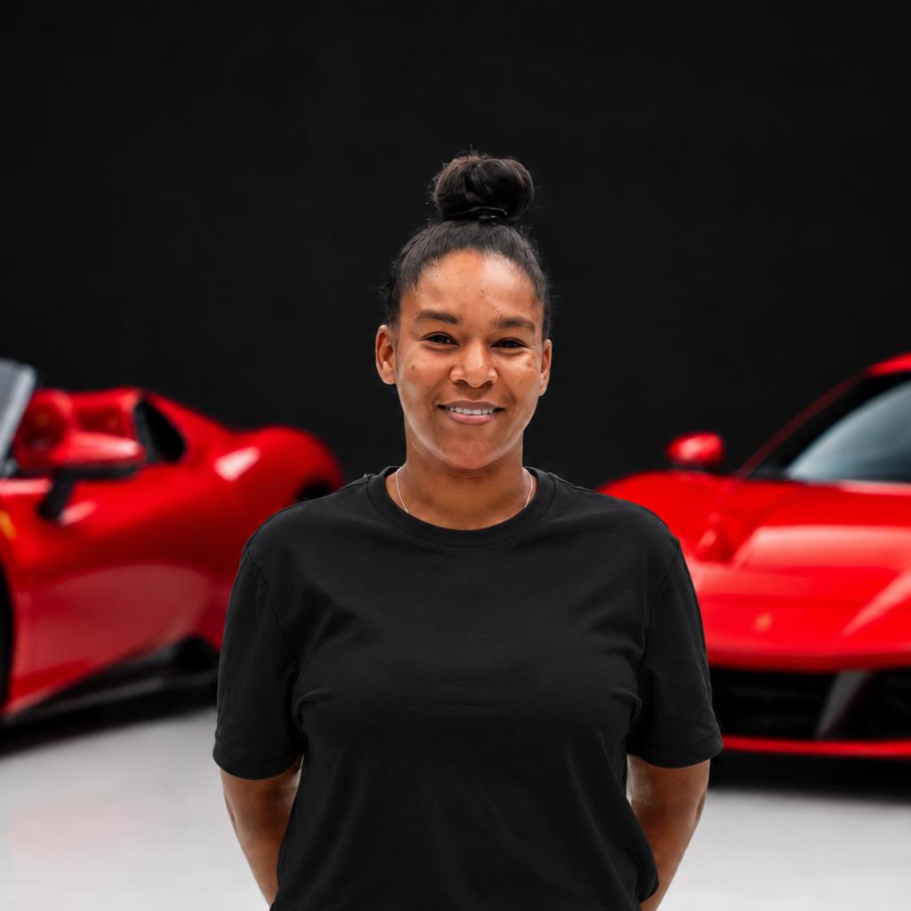 Shatheablackpng | Txtcharlie Portrait of a smiling woman with a top knot hairstyle, standing in front of red sports cars wearing a black T-shirt.